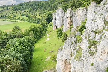 Felsformationen und grüne Landschaft mit Bäumen und Wiesen im Vordergrund.