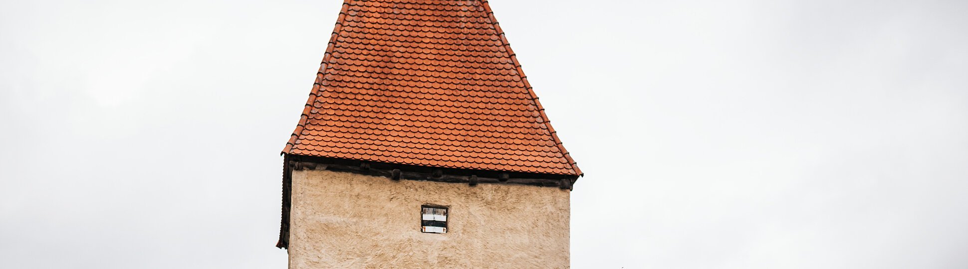 Zwei Radfahrer fahren an einem historischen Stadttor mit rotem Dach und Durchfahrt vorbei.