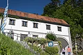Torbogenhaus in Wellheim Weißes Gebäude mit rotem Ziegeldach, bayerischer Flagge und zwei Personen vor einem Torbogen bei Sonnenschein