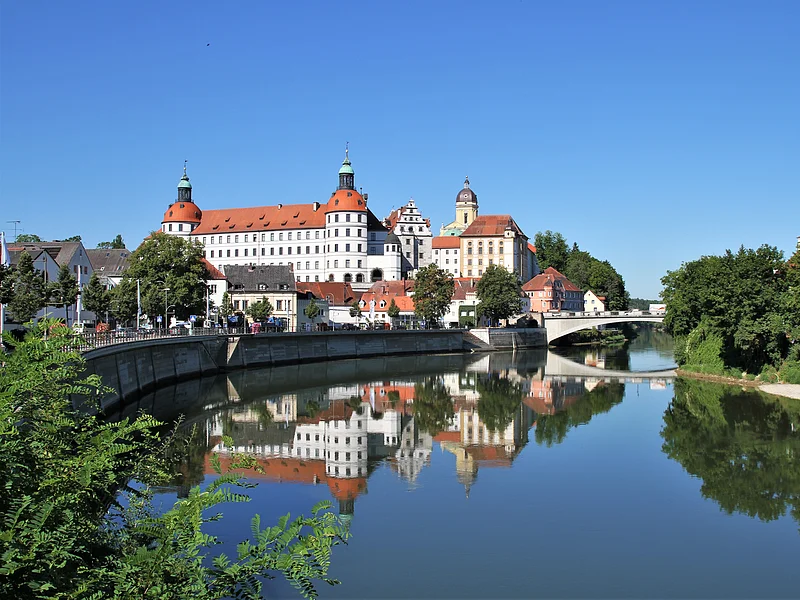 Schloss Neuburg Stadtansicht mit Schloss und Brücke, Spiegelung im Fluss, blauer Himmel, Bäume am Ufer